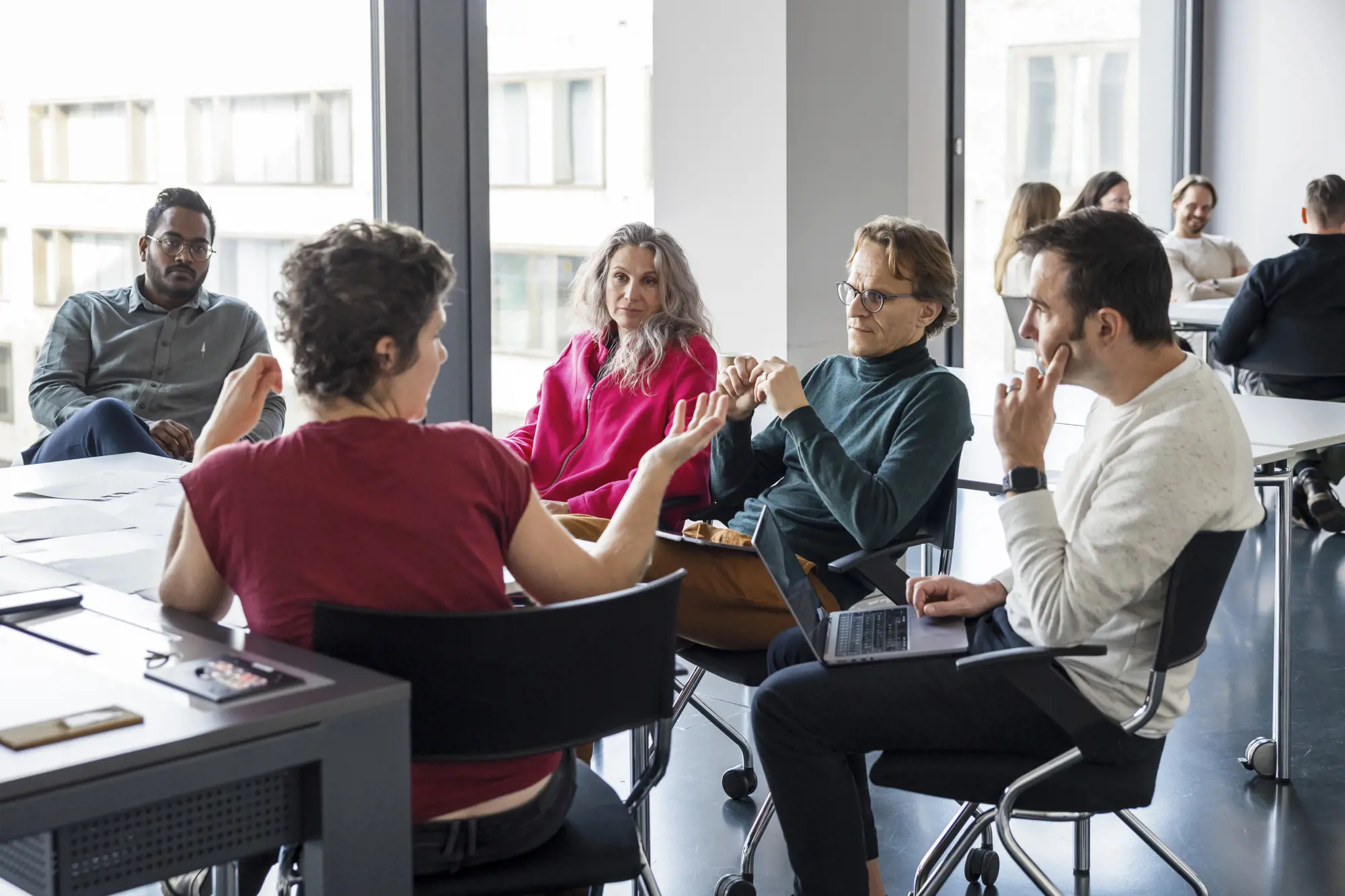 Eine Gruppe Menschen sitzt an einem Tisch und debattiert eine Sachfrage.