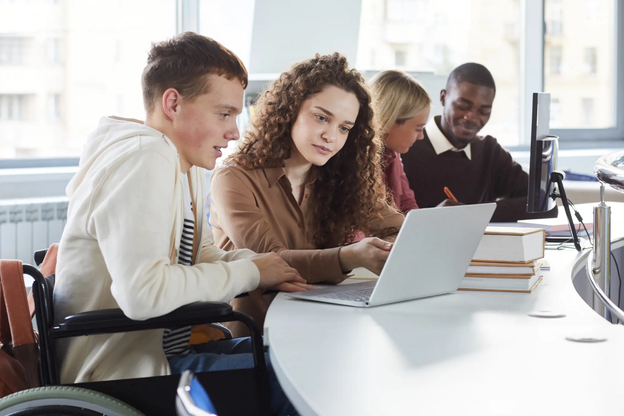Four people are sitting at a round table. They are working in pairs on computers.