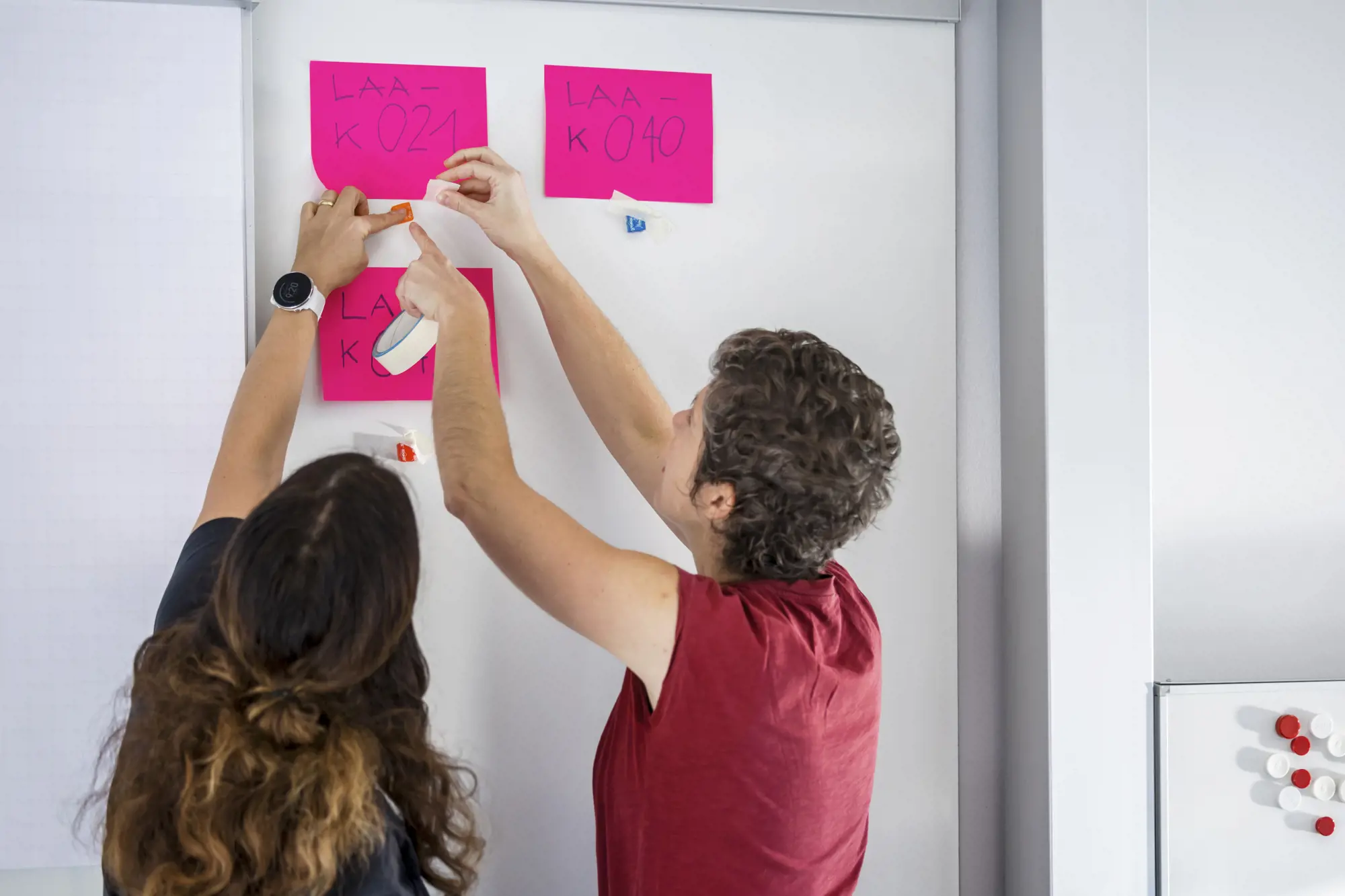 Two people work with post-its on a movable wall.