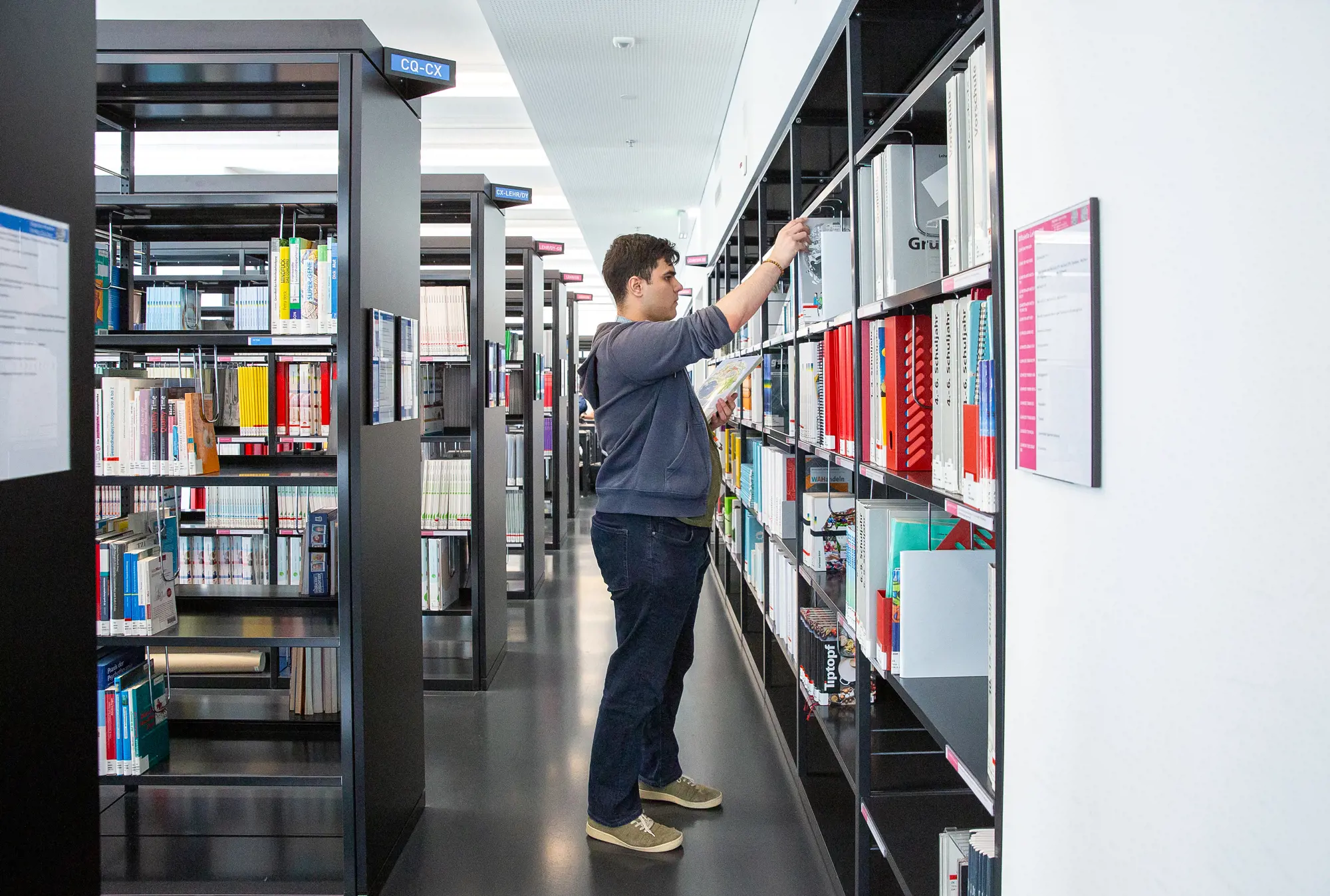 Ein Lernender Information und Dokumentation steht vor einem Bücherregal in der Bibliothek.