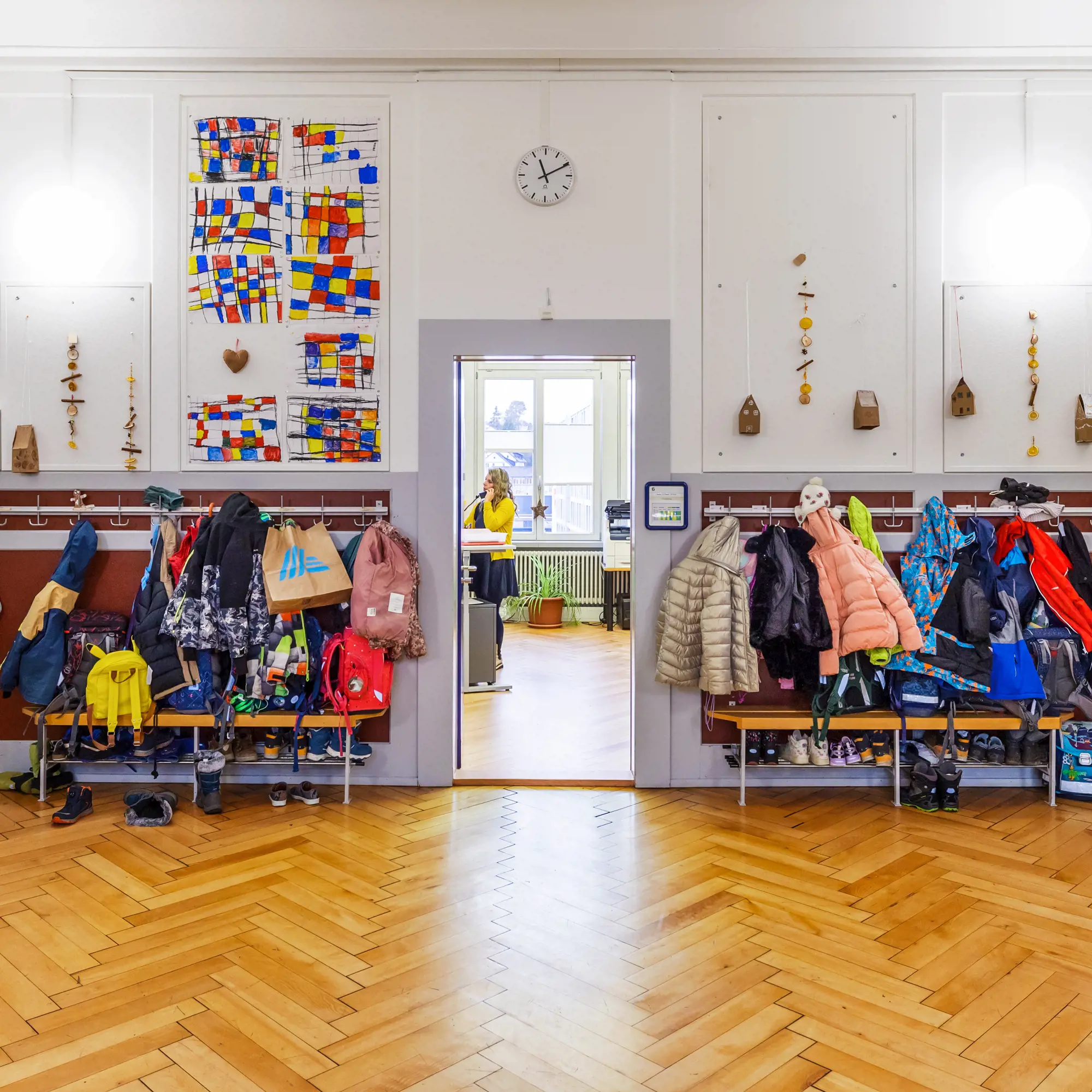 Farbenfroher und belebter Schulflur mit Garderoben und Kinderkunst.