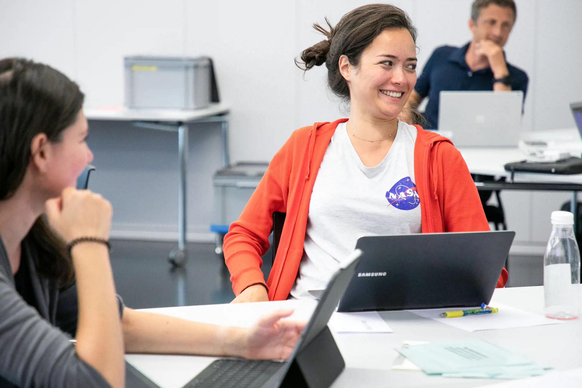 Eine Lehrerin sitzt vor einem aufgeklappten Laptop. Sie lächelt.