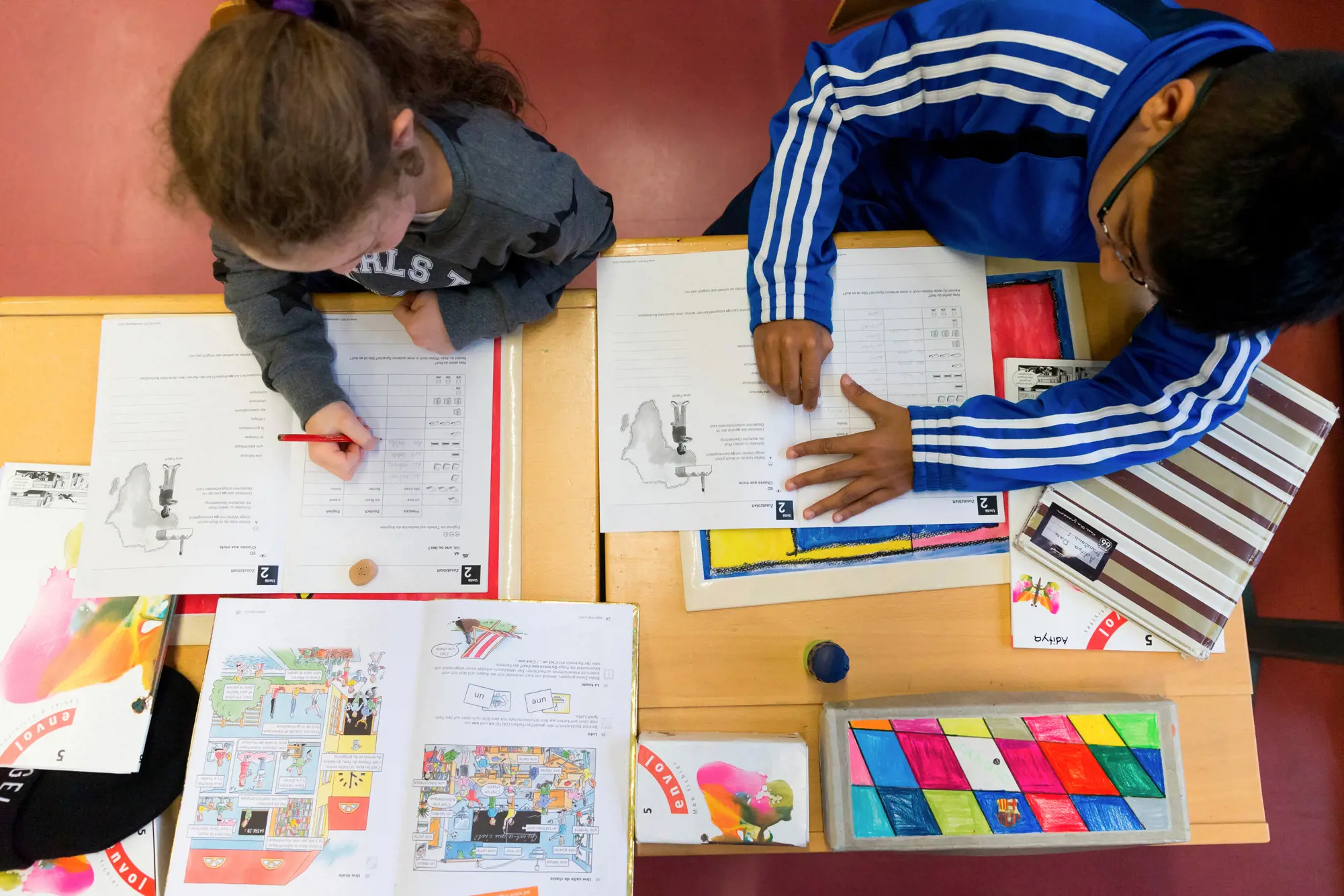 A girl and a boy, seen from above, are each working on a task in their workbook.