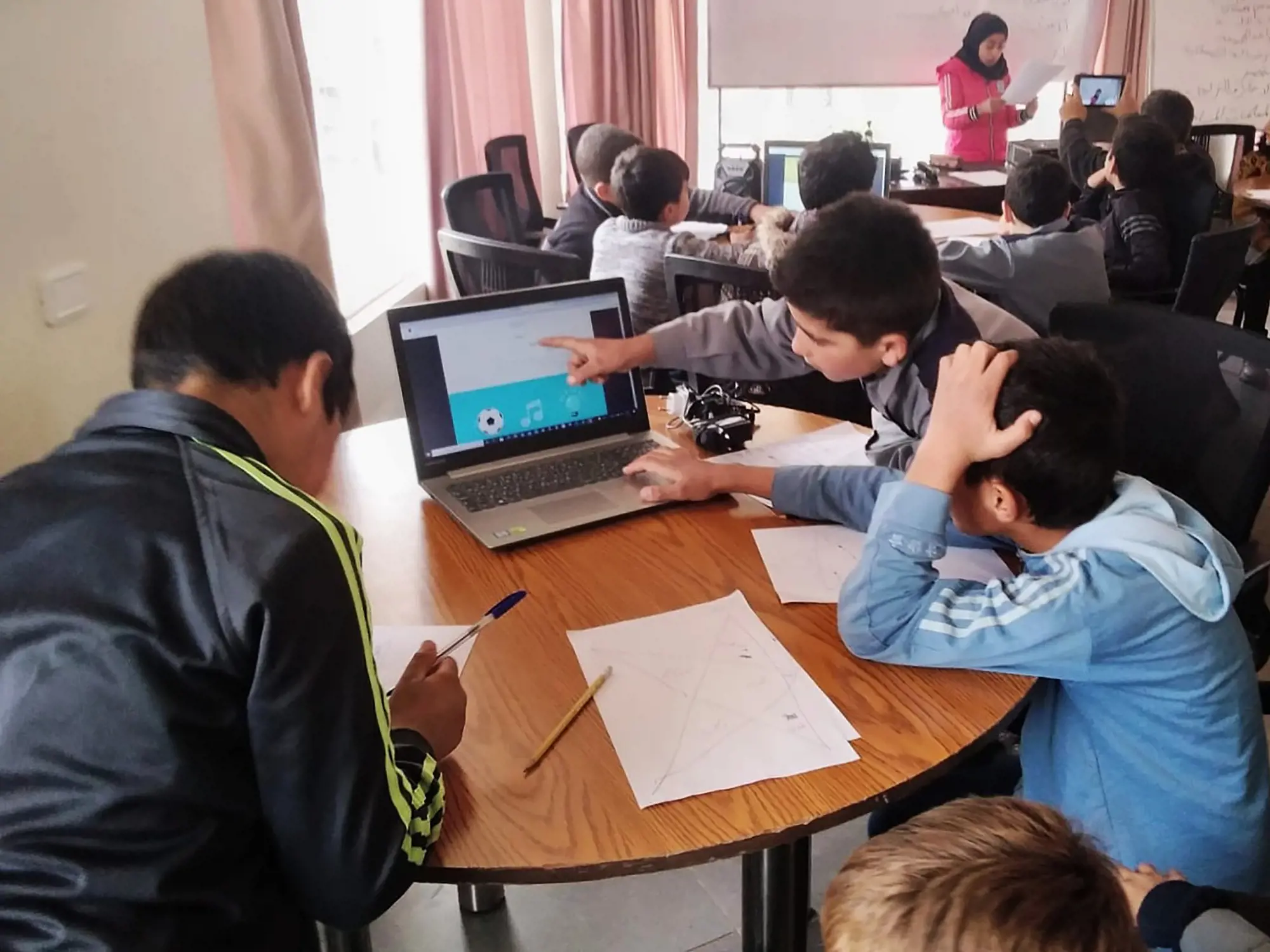 Kinder lernen mit Computern an einem runden Holztisch.
