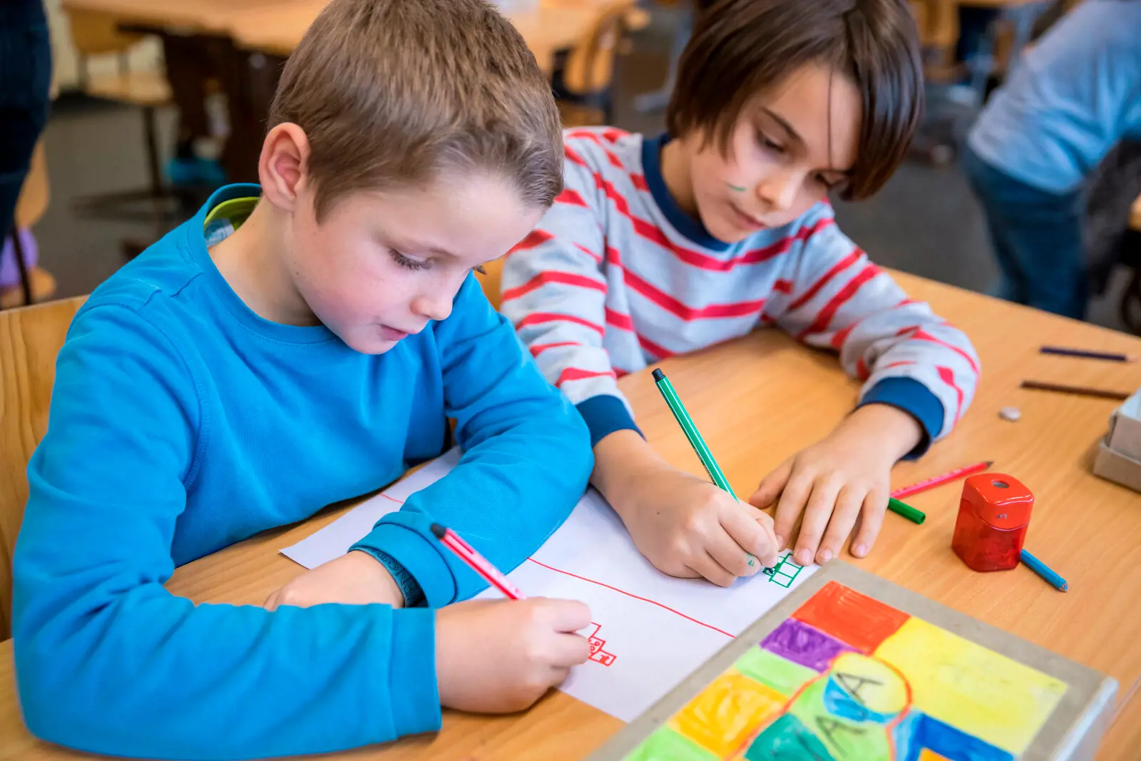 Two boys sit next to each other and paint.