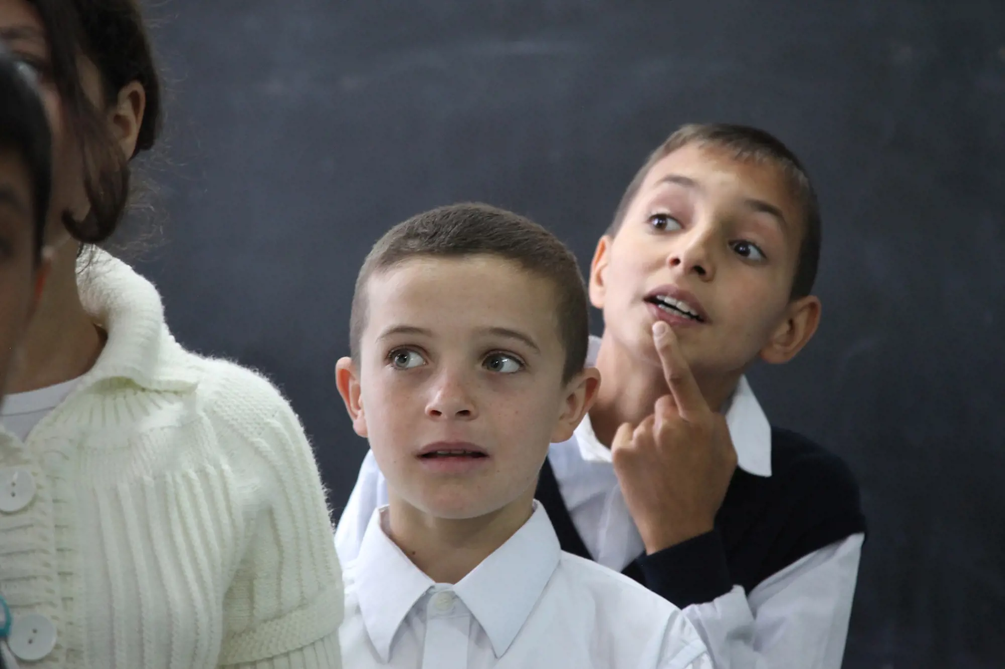 Three boys stand behind each other and observe something at school.