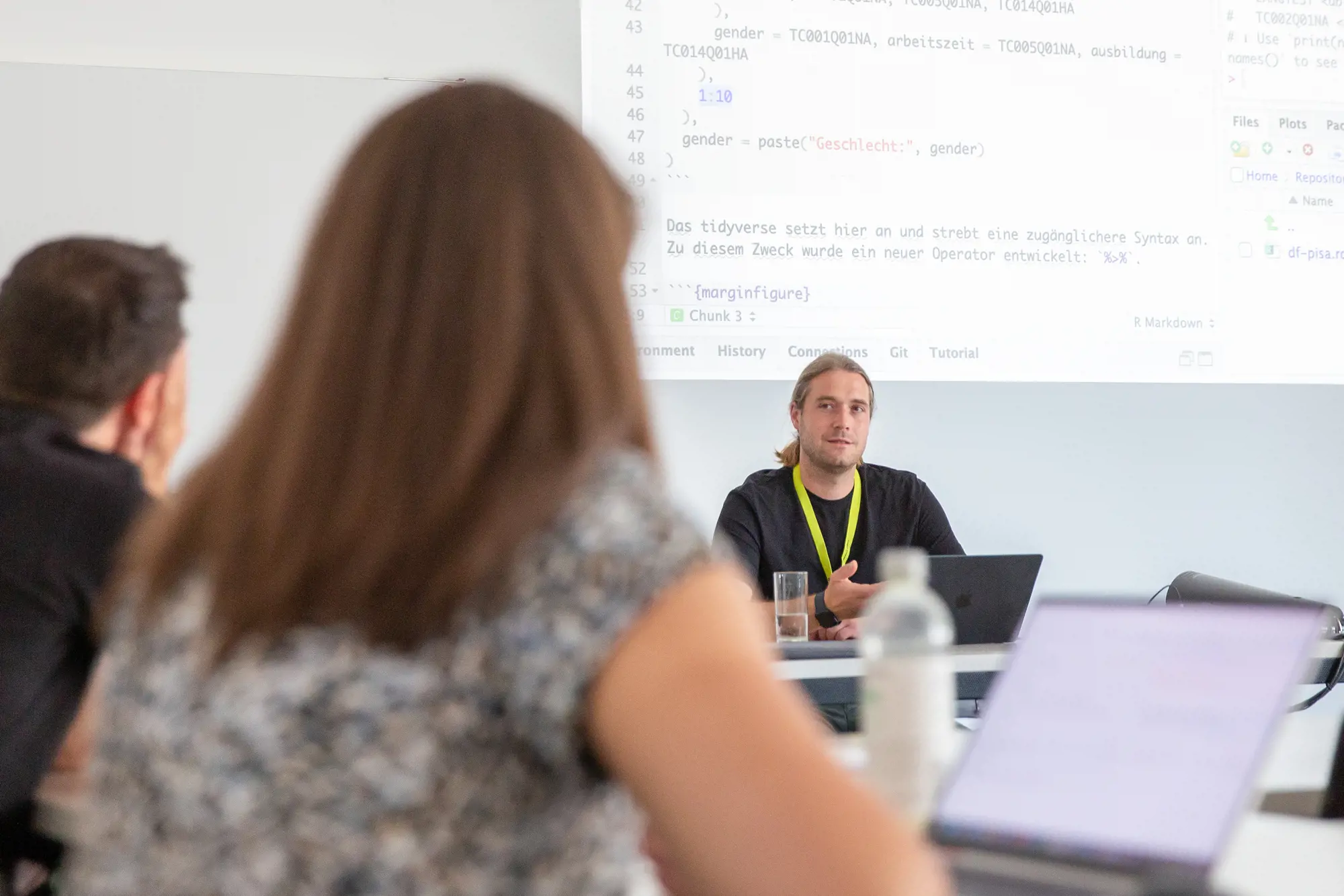 A researcher sits in front of a screen and presents his research results to listeners who are out of focus from behind.
