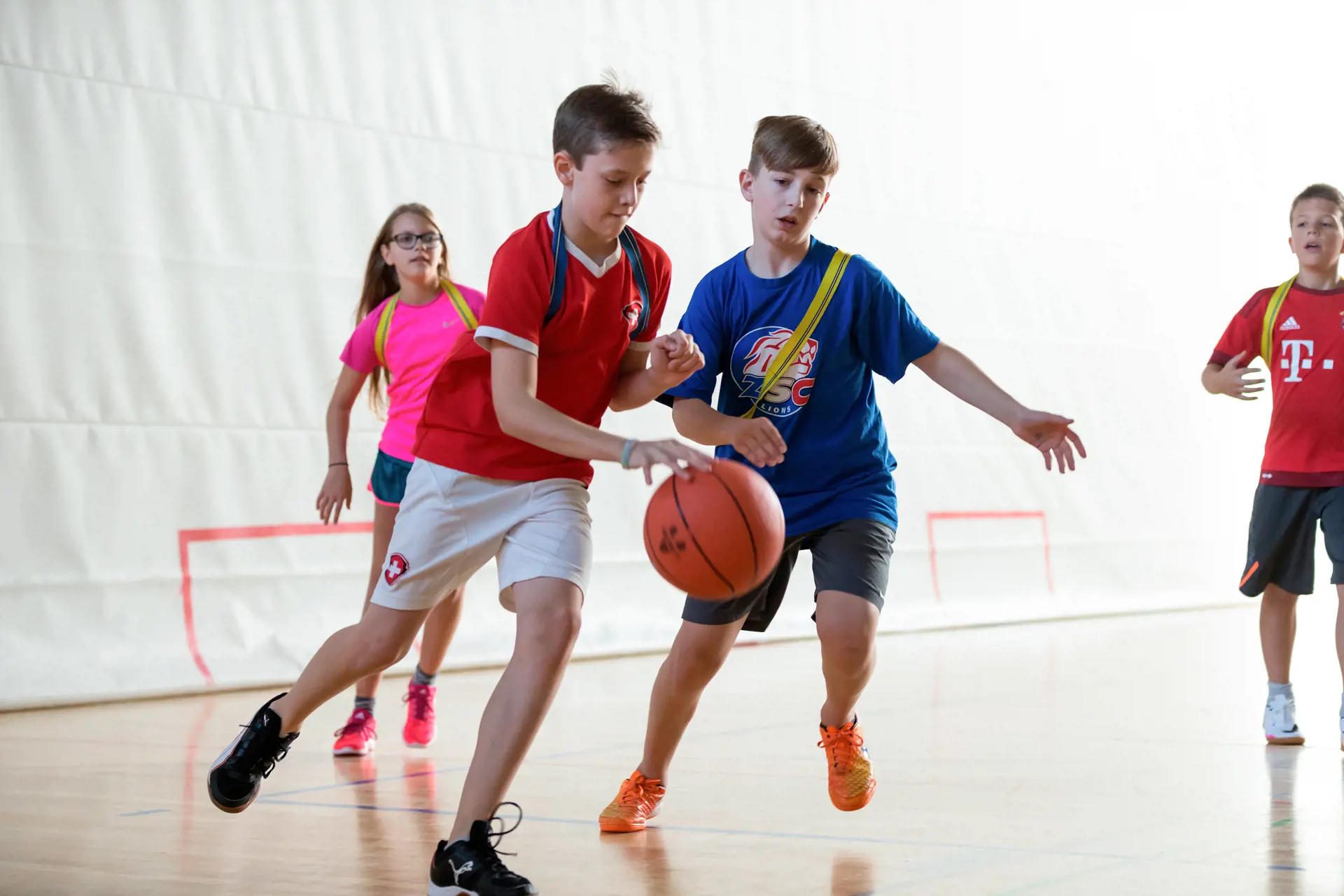 Four schoolchildren play basketball in a gym.