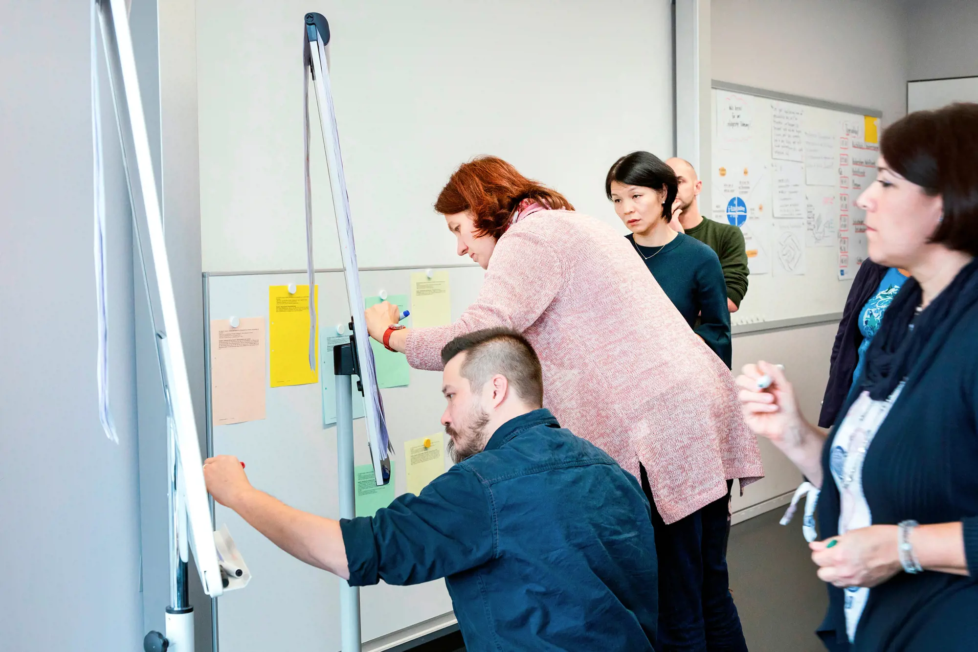 Zwei Frauen und ein Mann machen Notizen und hängen Zettel an einen Flipchart.