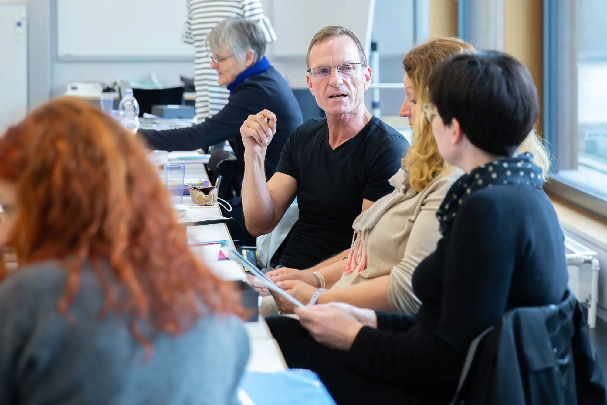 Seminarteilnehmer:innen sitzen nebeneinander und diskutieren. Im Fokus ist ein Mann, der gestikuliert.