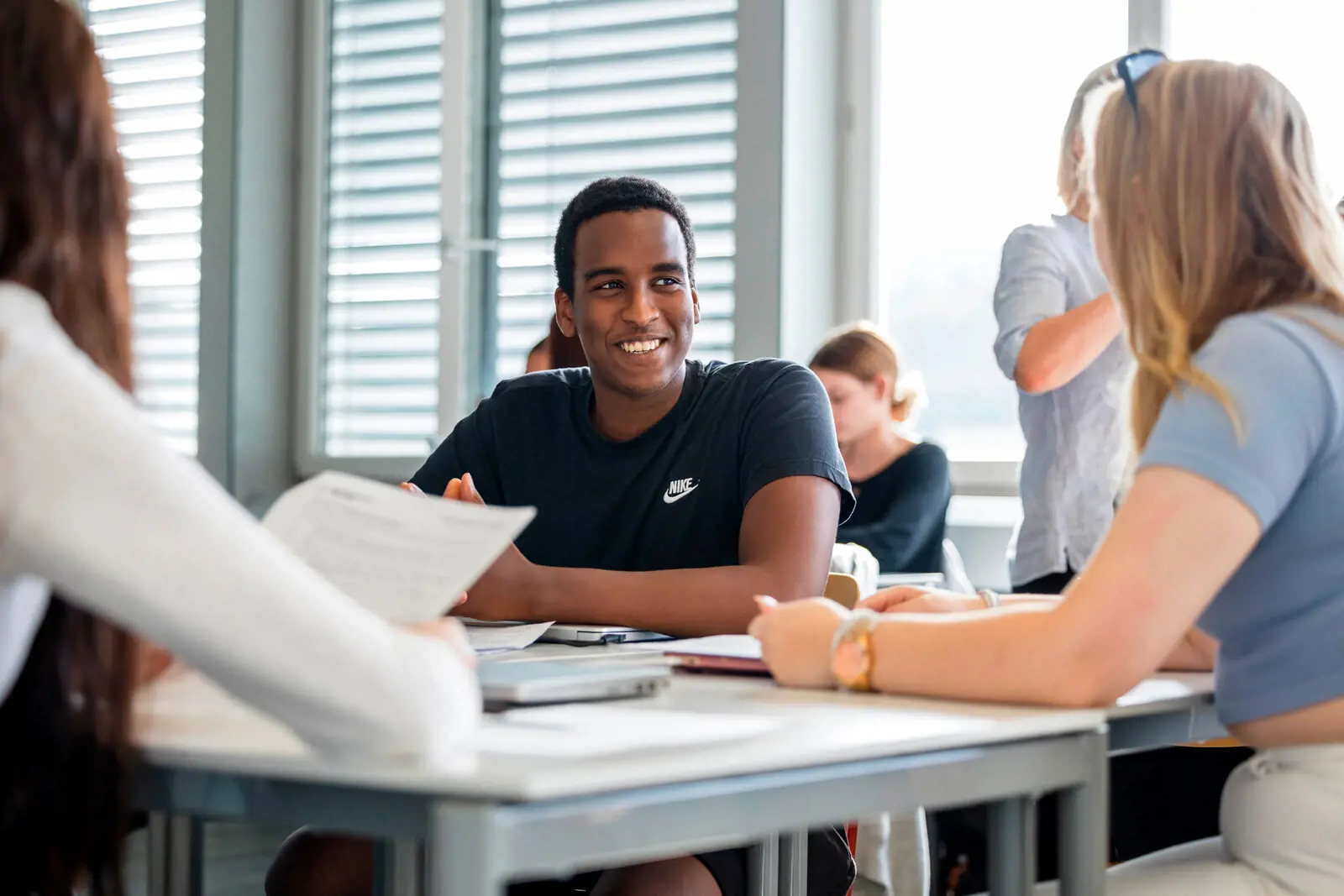 Ein Berufsschüler sitzt mit seinen Mitschüler:innen an einem Tisch und lächelt.