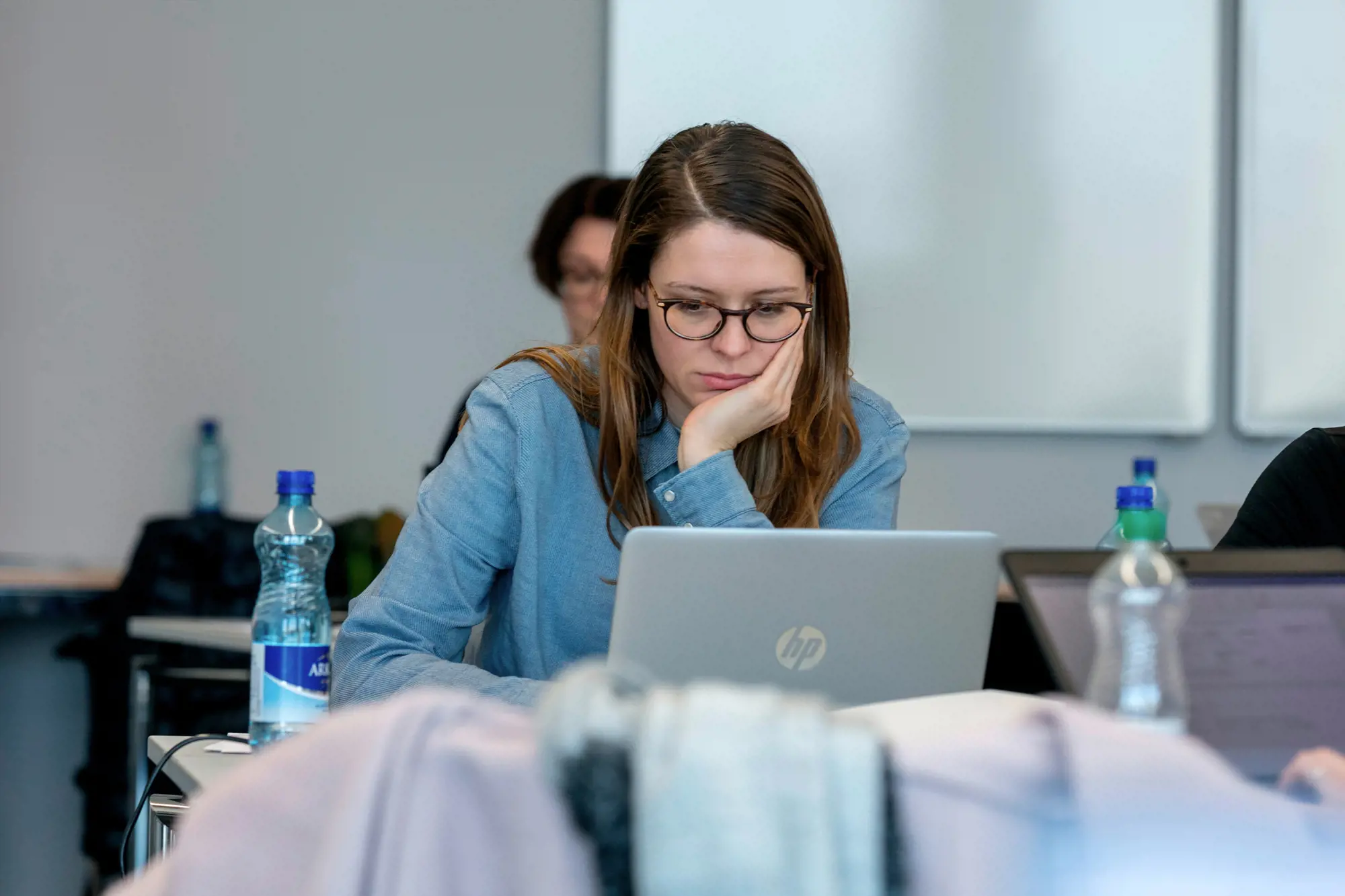Eine Frau sitzt vor einem Laptop. Sie stützt den Kopf auf ihrer Hand auf.