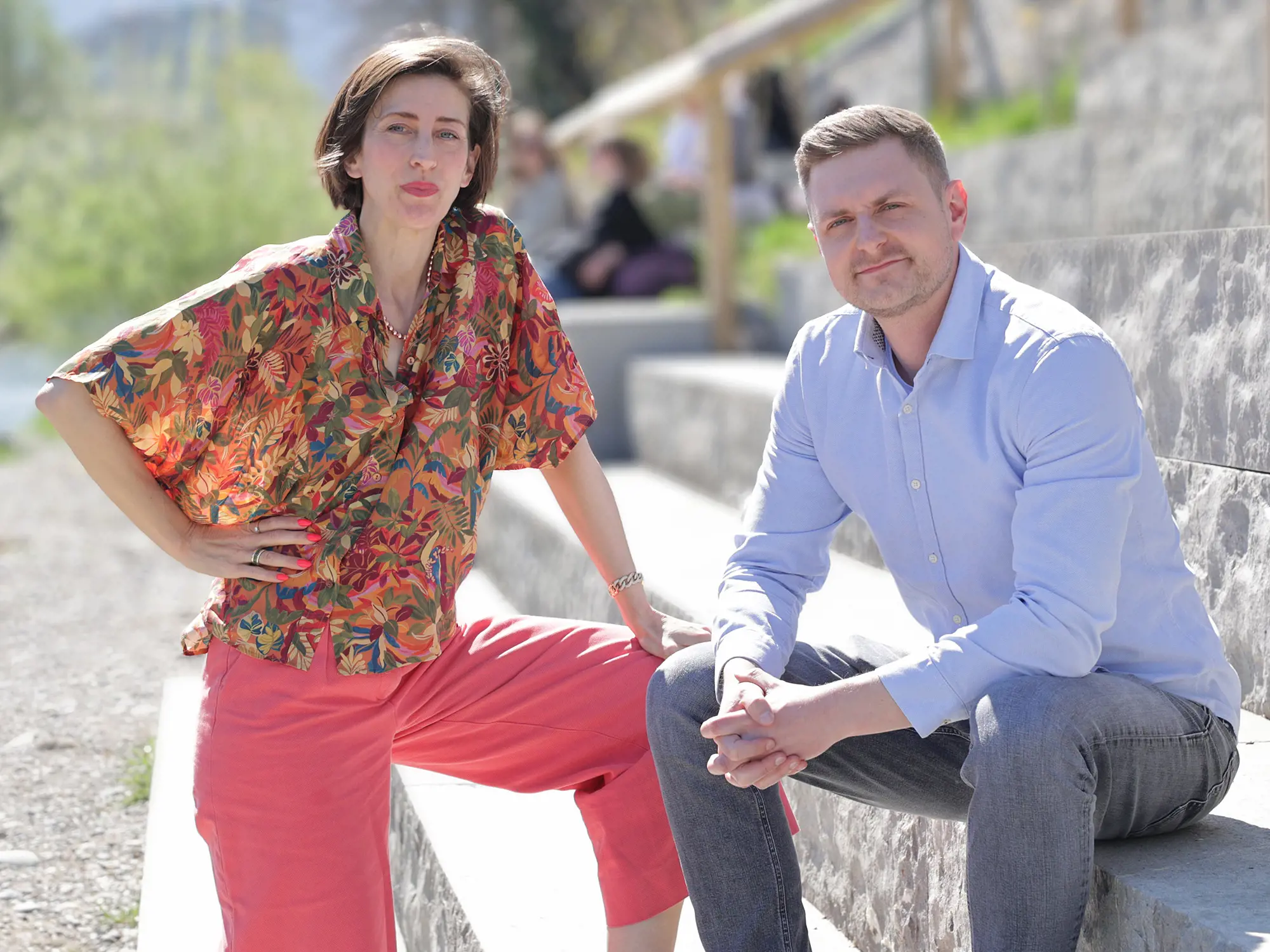 Charlotte Axelsson und Gabriel Flepp, Lehrgangsleitende CAS Education Futurist, sitzen an einer steinernen Uferpromenade im Freien; im Hintergrund sind Wasser und Bäume zu sehen.