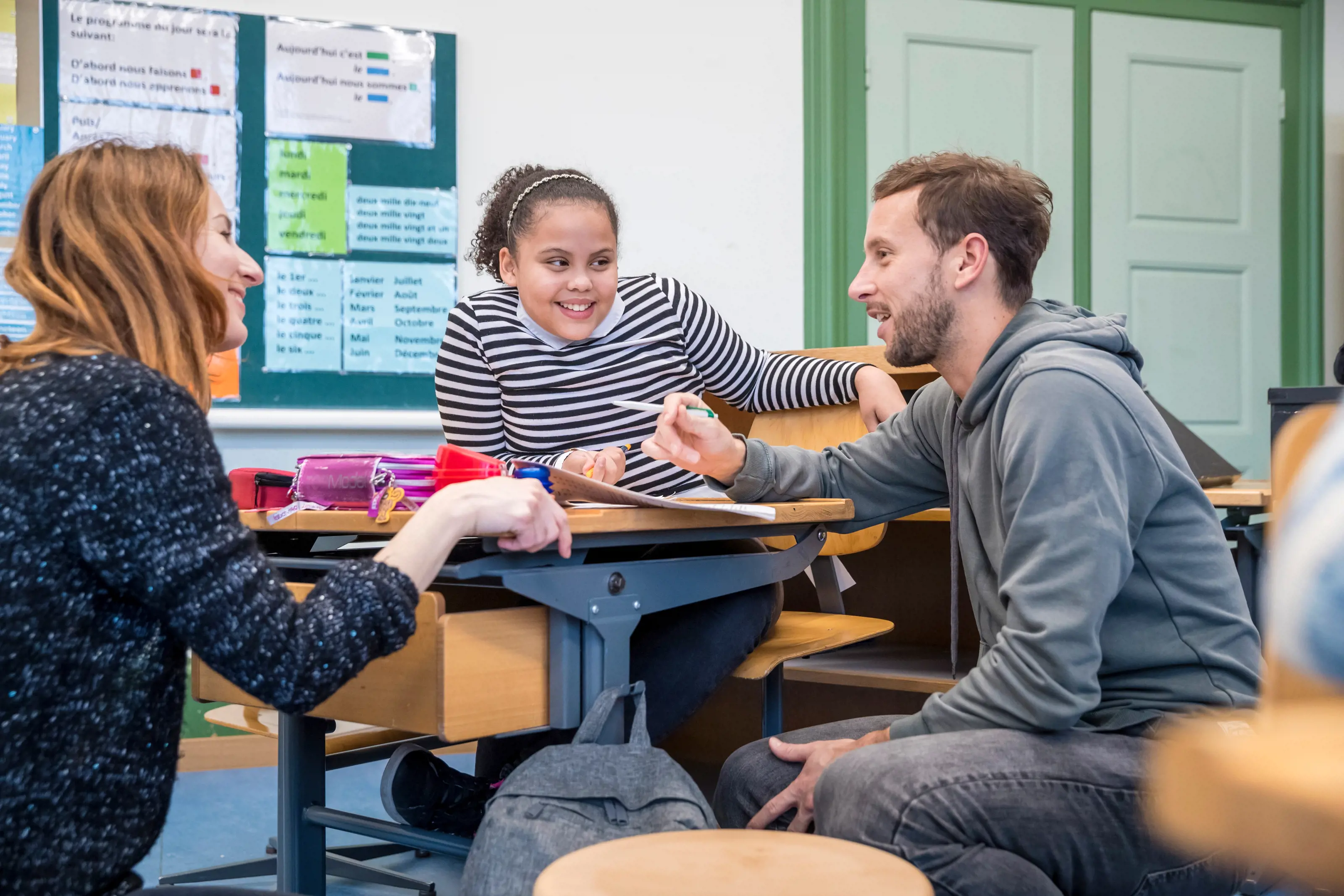 Eine Lehrerin, ein Lehrer und eine Schülerin sitzen sich gegenüber und sprechen miteinander.