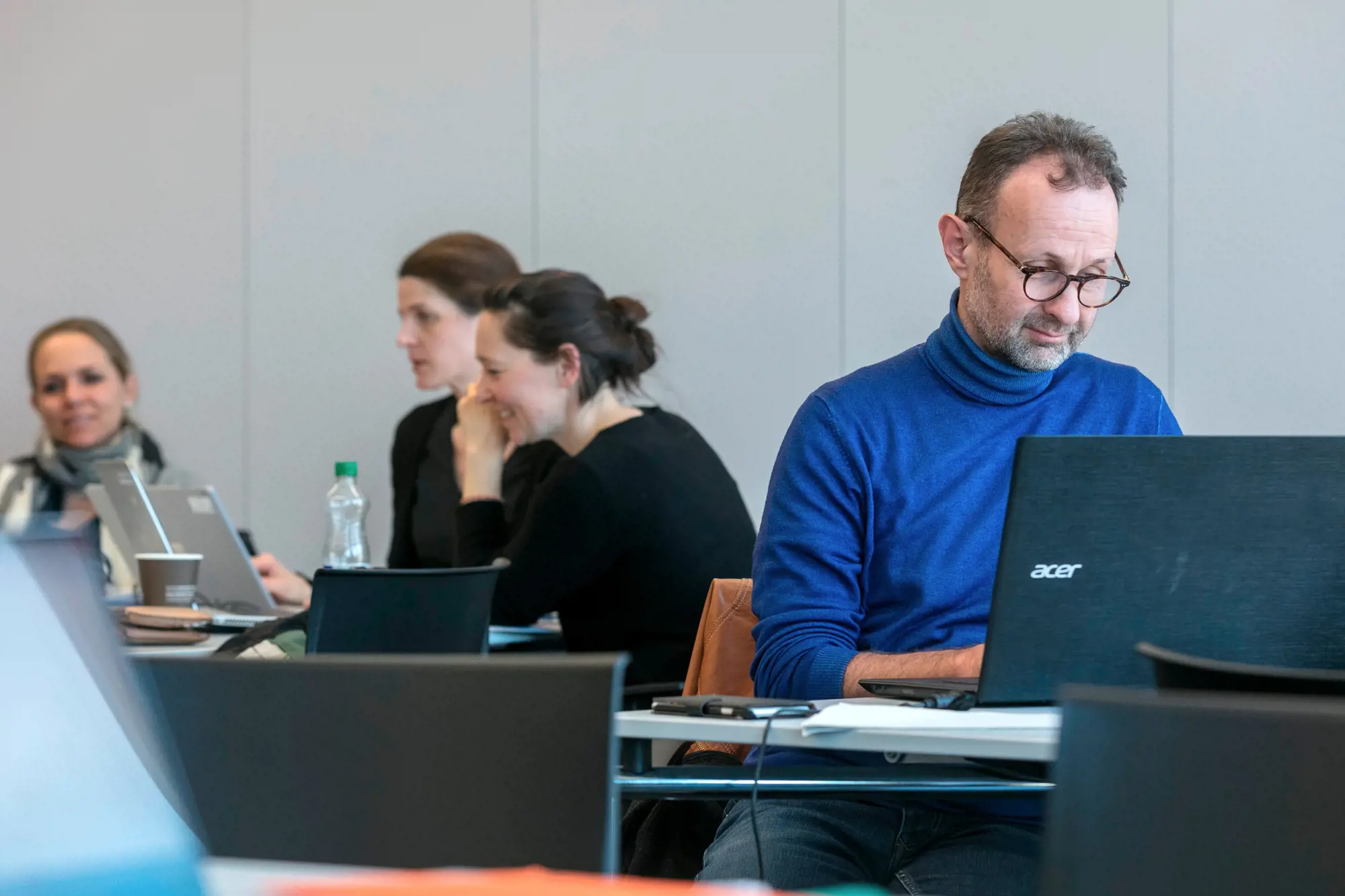 Frauen und Männer sitzen an Tischen und unterhalten sich oder schauen in den Laptop.