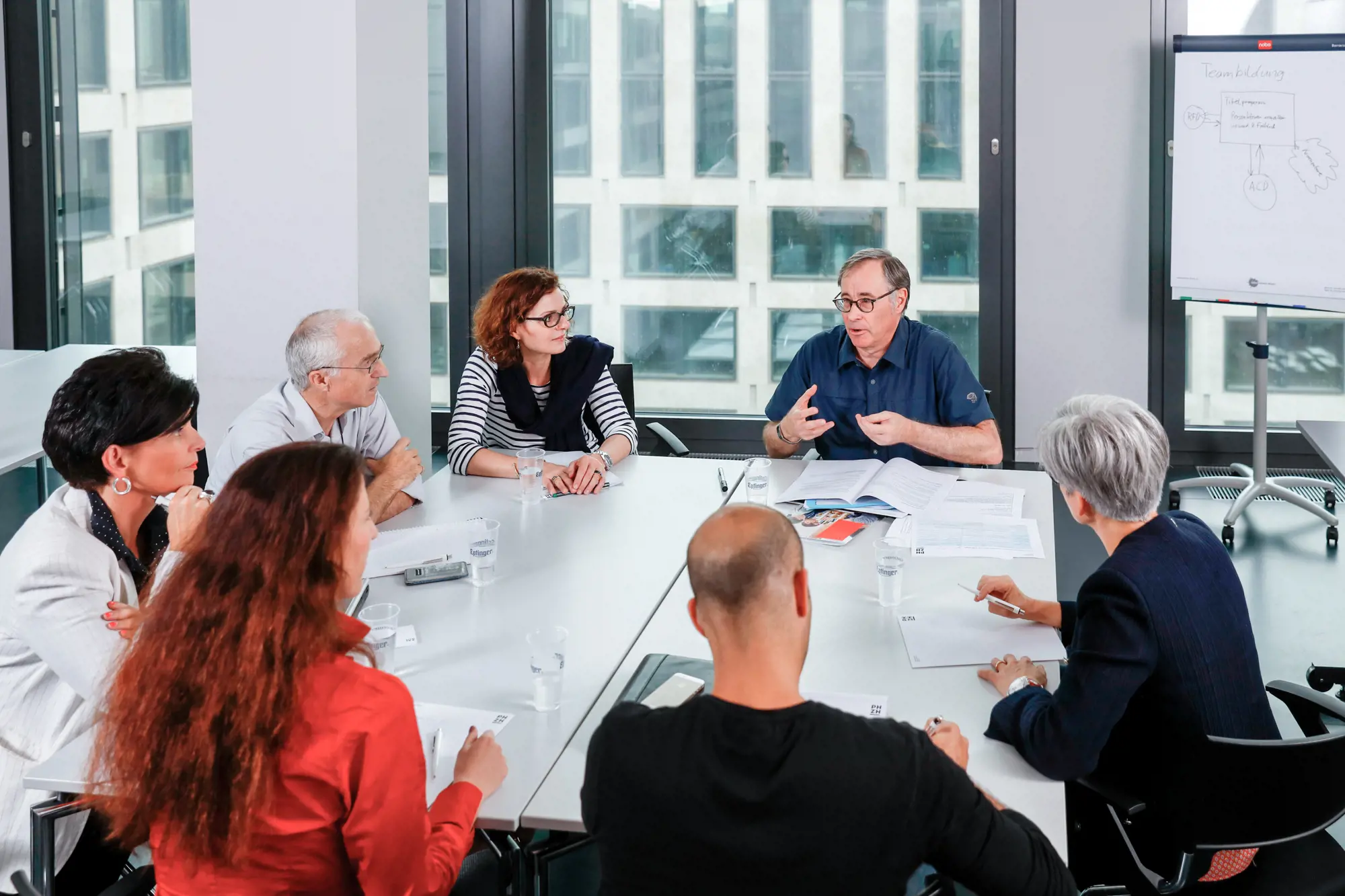 Eine Gruppe von sieben Personen bespricht an einem Tisch ein Thema.